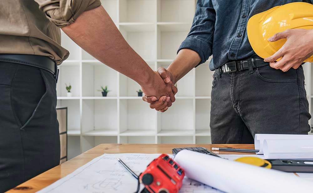 Black sedan parked by a glass building with trees and hills in the background.